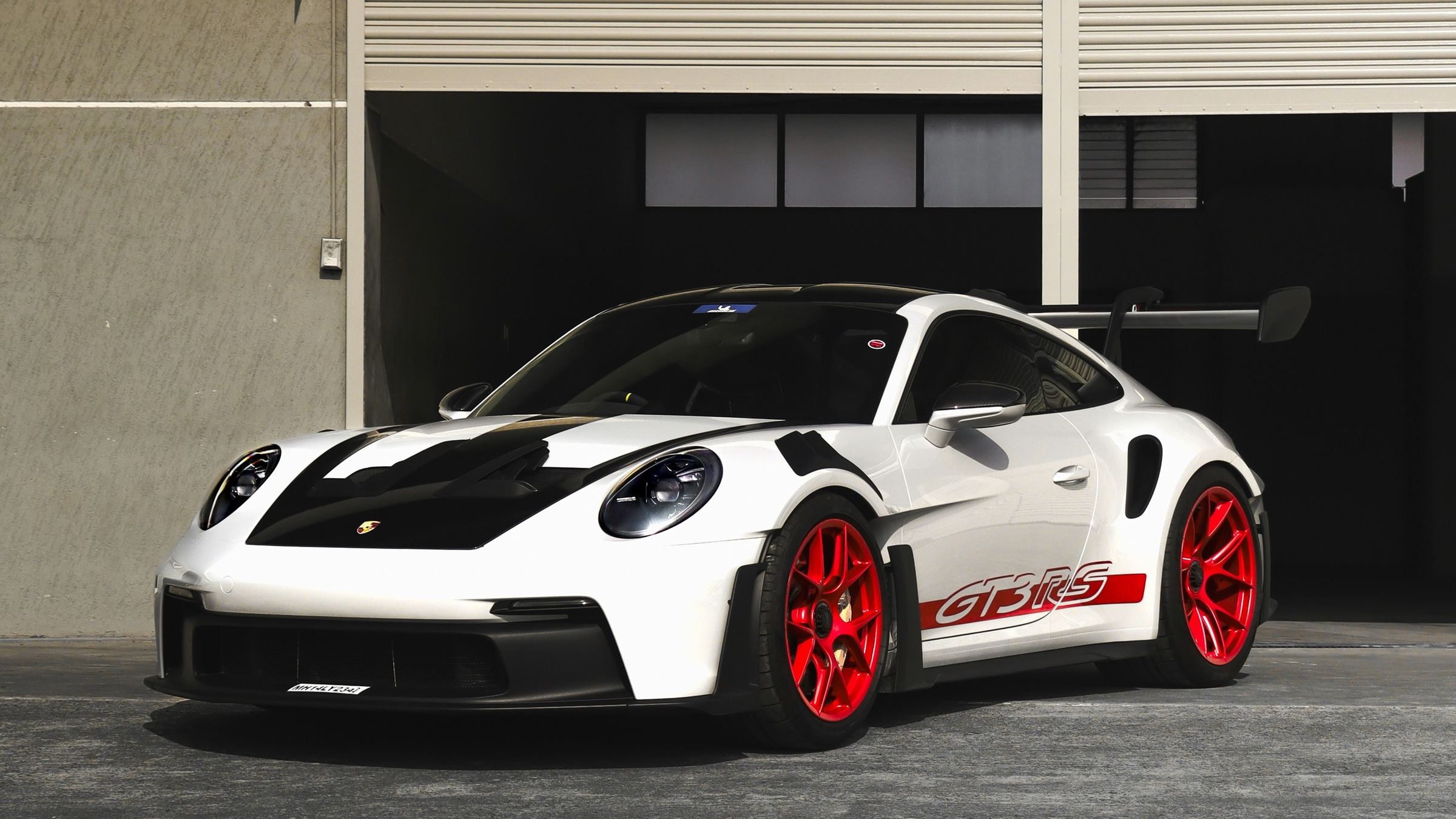 White Porsche 911 GT3 RS with red wheels parked outside a garage